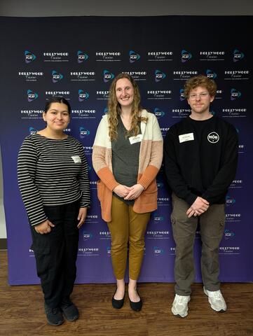three TEA Lab members at the Hollywood Columbus Casino, in front of a backdrop with their logo.