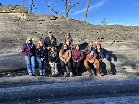 9 people pose on glacially carved rock.