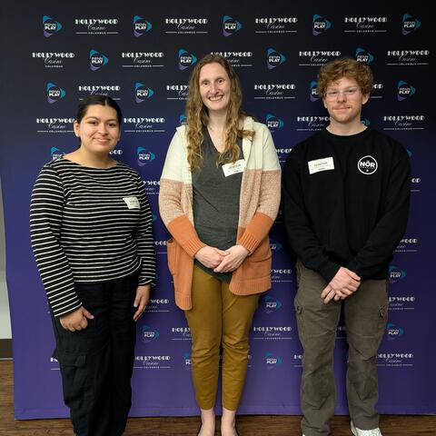 three TEA Lab members at the Hollywood Columbus Casino, in front of a backdrop with their logo.