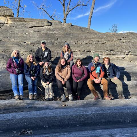 9 people pose on glacially carved rock.